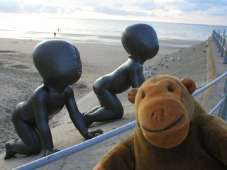 Mr Monkey looking at two giant babies crawling up the Middelkerke seawall