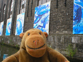 Mr Monkey passing abstract paintings on a wall by the canal